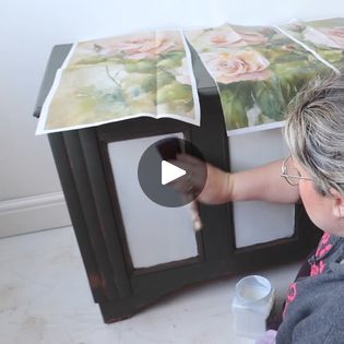 a woman is painting flowers on the side of a cabinet