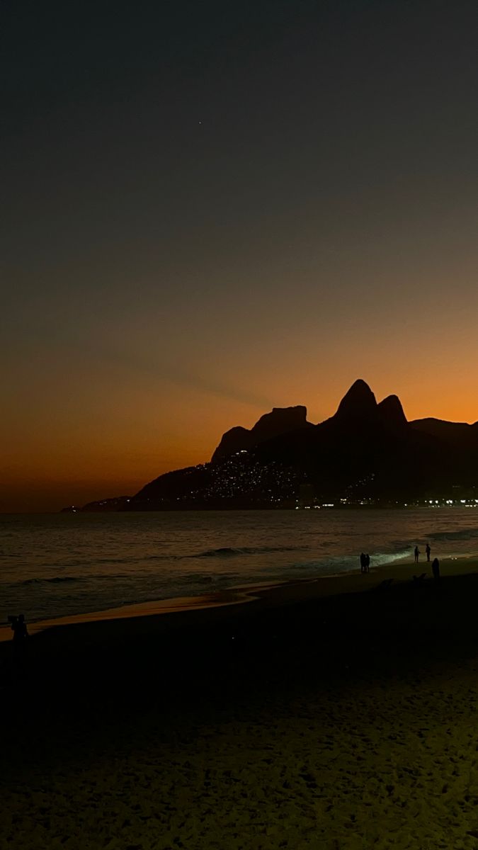 people walking on the beach at sunset with mountains in the background