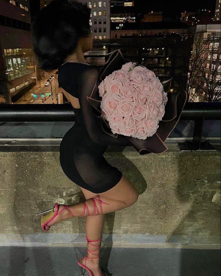 a woman holding a bouquet of flowers on top of a building in the city at night