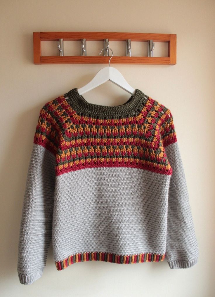 a sweater hanging on a coat rack in front of a white wall with a wooden hanger