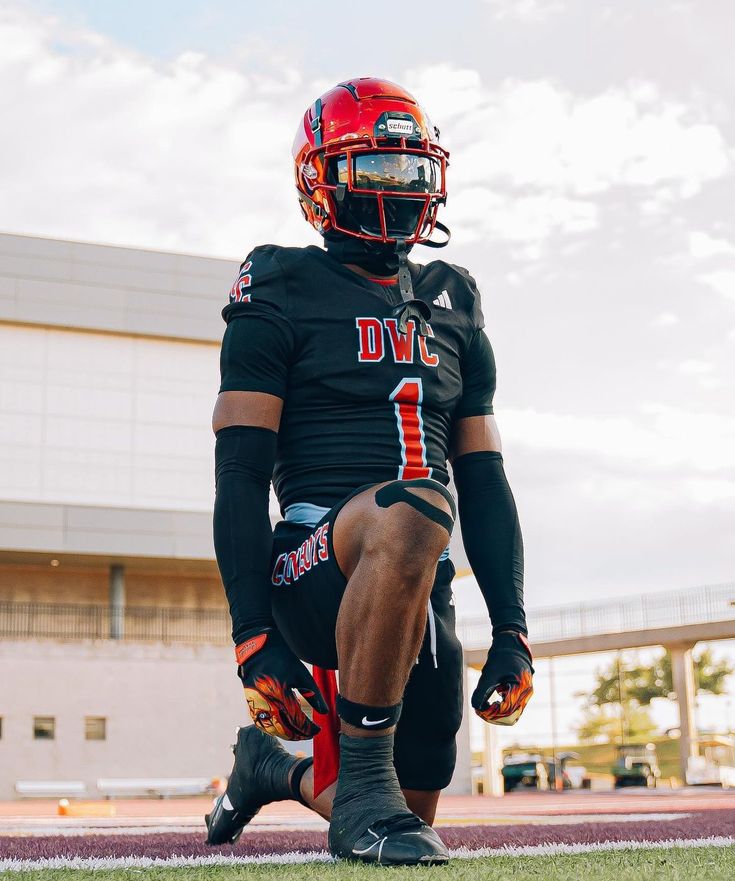 a football player sitting on the sidelines with his foot in the air while wearing black and red uniform