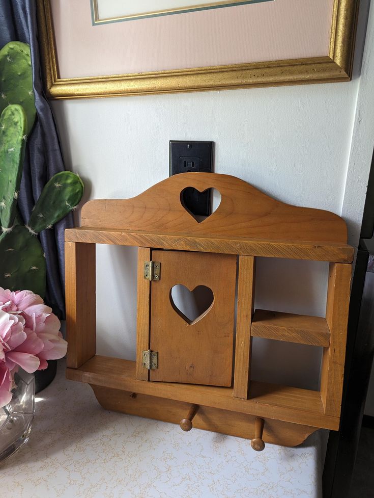 a wooden birdhouse with a heart cutout on the front and sides, sitting next to a potted plant