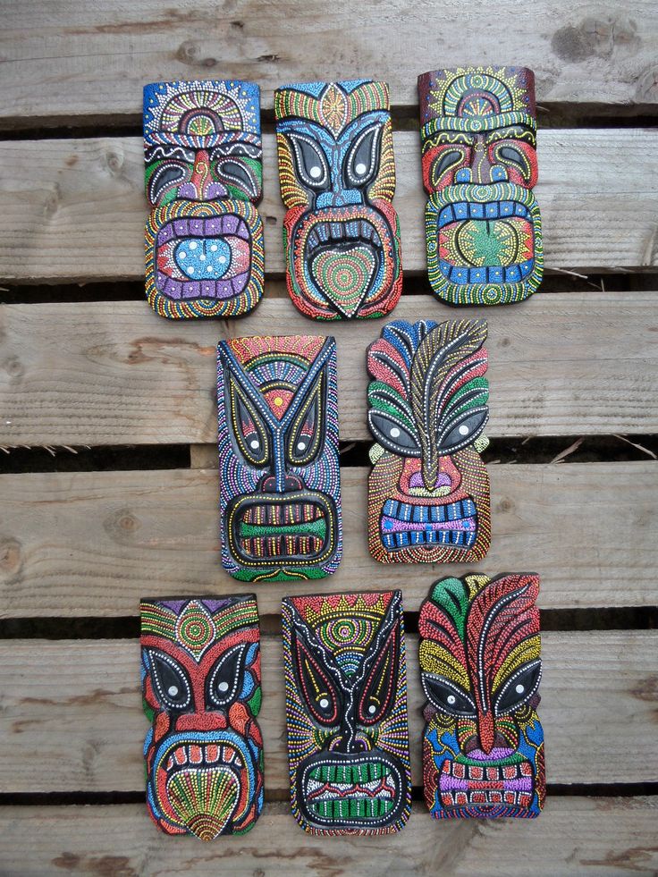 six hand painted tiki masks sitting on top of a wooden table