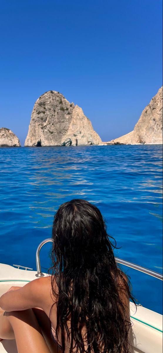 a woman sitting on the back of a boat looking out at an island in the ocean