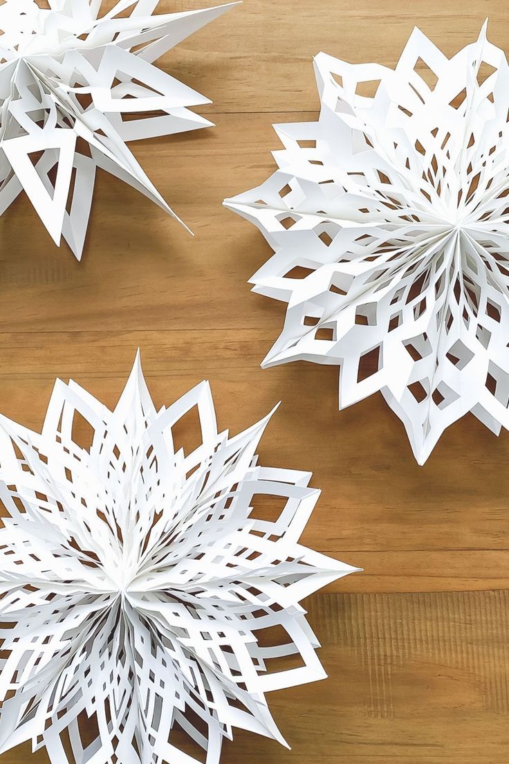 three white paper snowflakes sitting on top of a wooden table next to each other