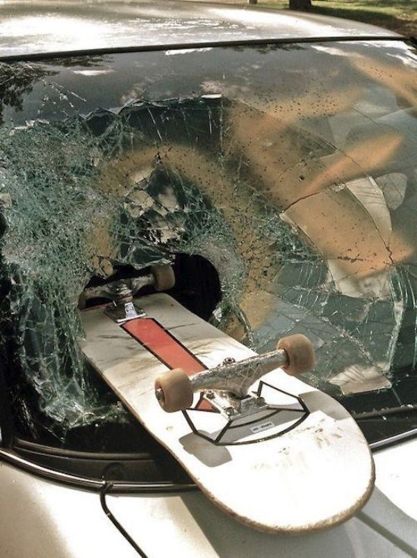 a skateboard that is sitting in the windshield of a car with it's front window shattered