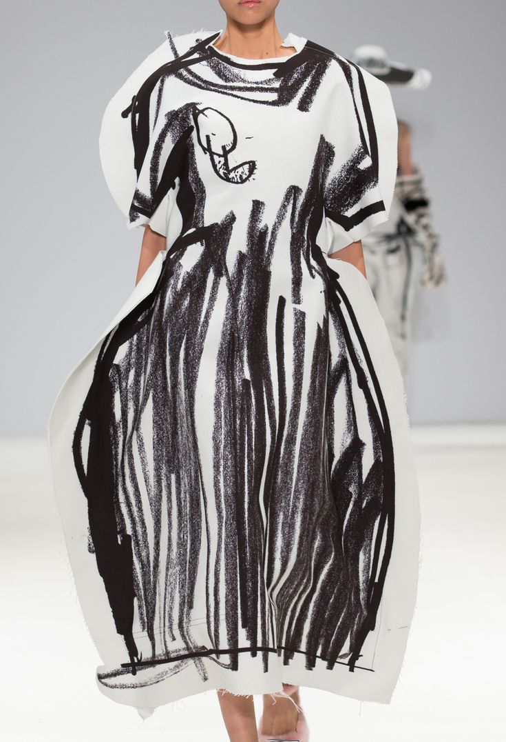 a woman walking down a runway wearing a dress with black and white designs on it