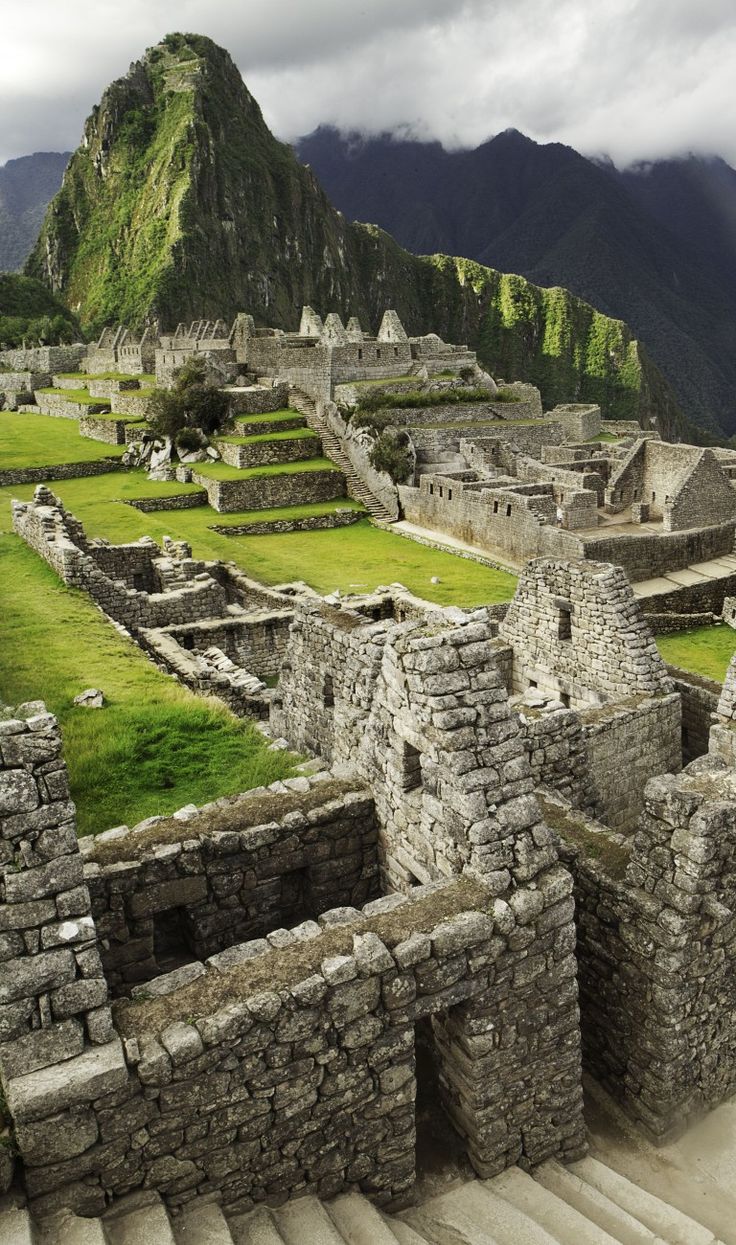 an old stone building with steps leading up to it and mountains in the background,