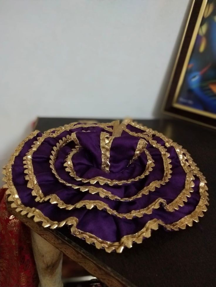 a purple and gold hat sitting on top of a wooden table next to a painting