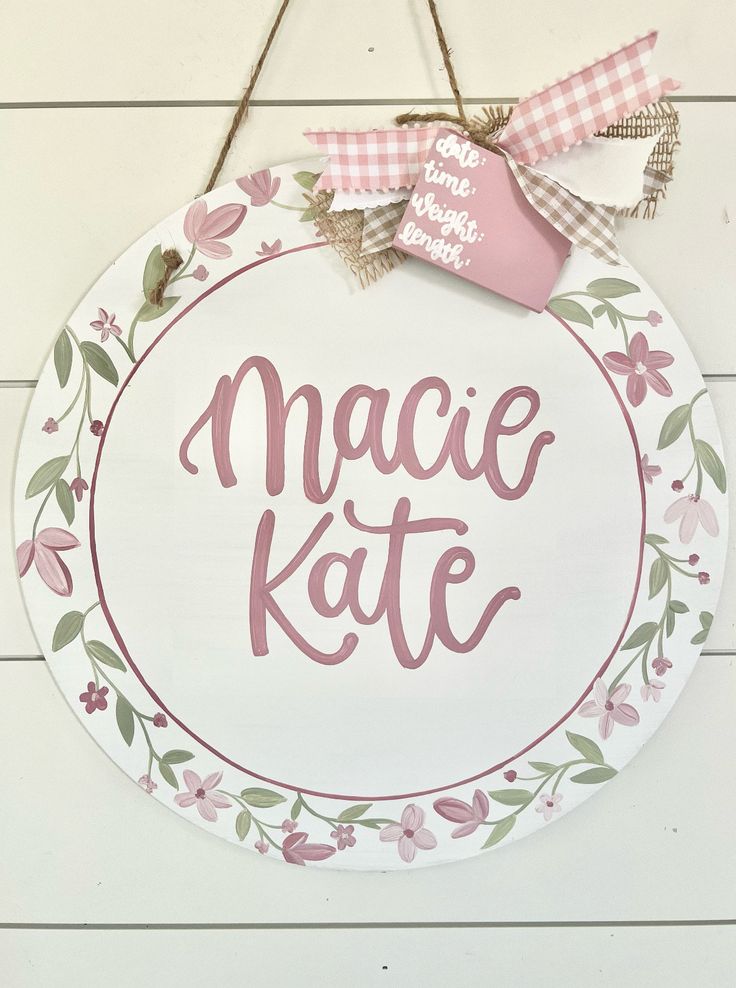 a sign that says macie kate hanging on a wall with pink and white flowers