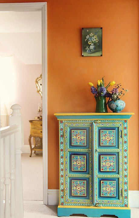 an orange and blue cabinet with flowers on top in a room that has white stairs