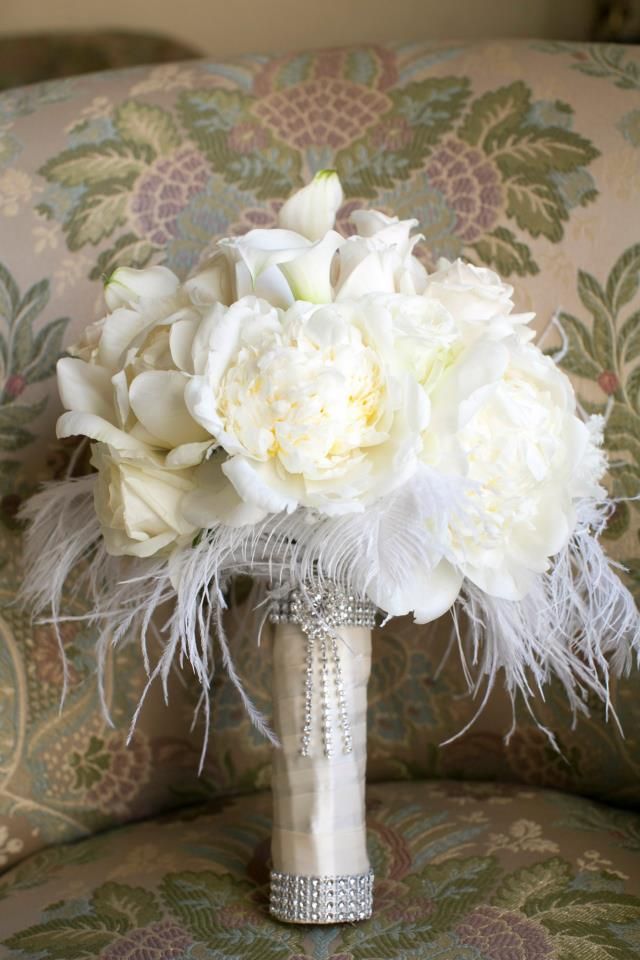 a bridal bouquet with white flowers and feathers on a chair in front of a couch