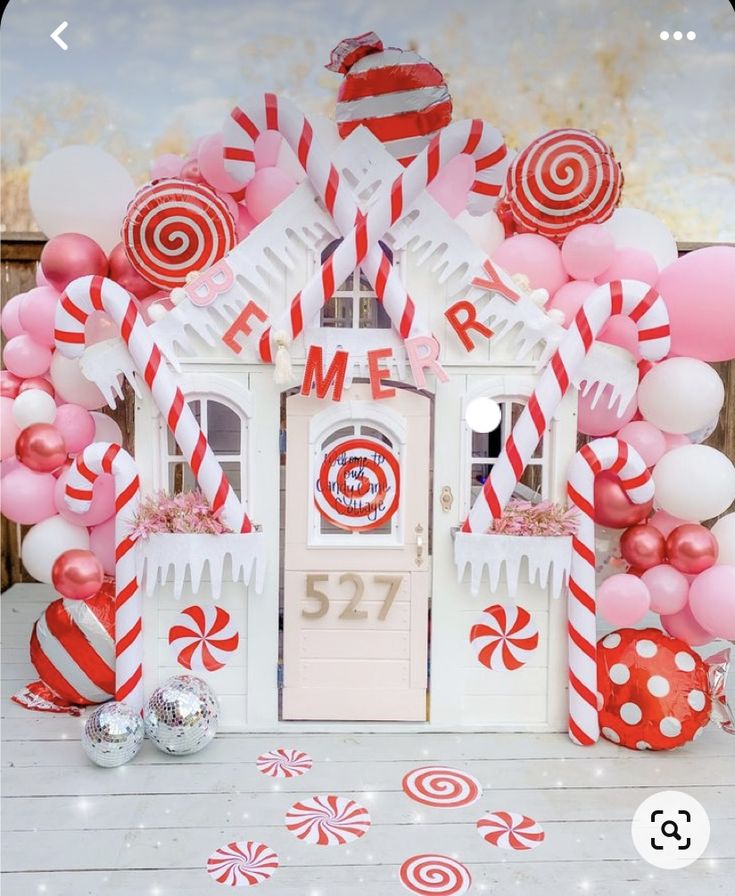 a white and red candy house surrounded by balloons