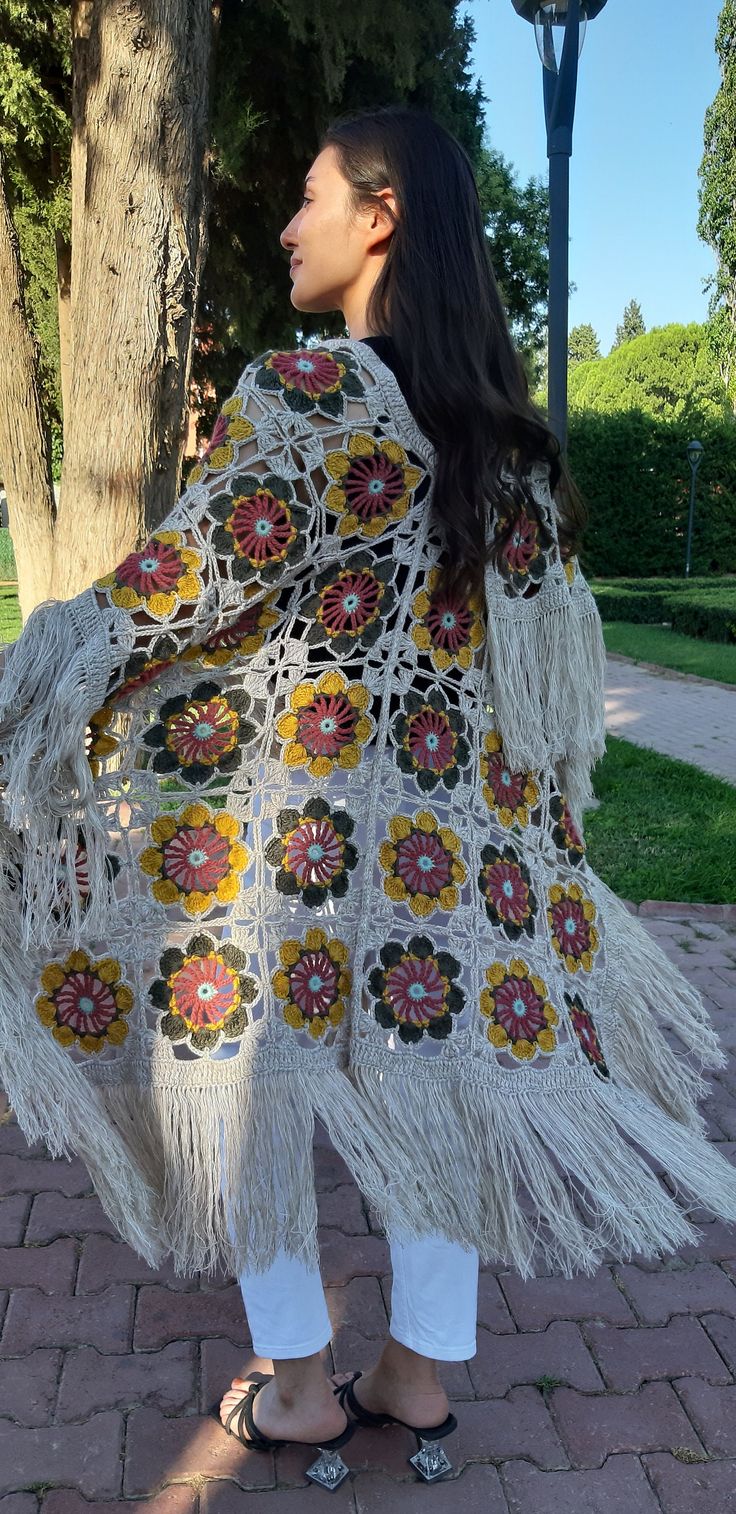 a woman is standing in front of a tree wearing a crocheted shawl