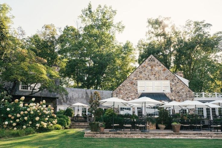 an outdoor dining area with tables and umbrellas in front of a stone building surrounded by trees