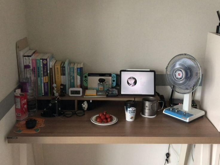 a desk with a fan, books and other items on it