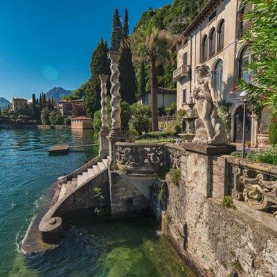 an old building on the edge of a body of water with trees and bushes around it