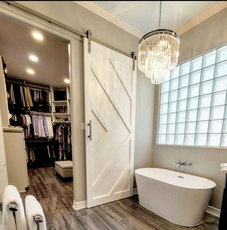 a white bath tub sitting next to a walk in closet under a chandelier