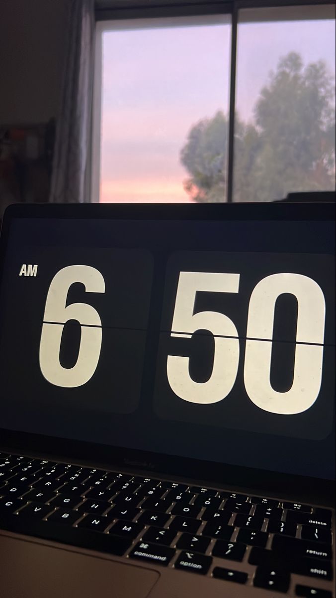 an alarm clock sitting on top of a laptop computer next to a window with trees outside