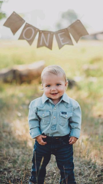 a little boy standing in the grass with his hands on his hips and looking at the camera