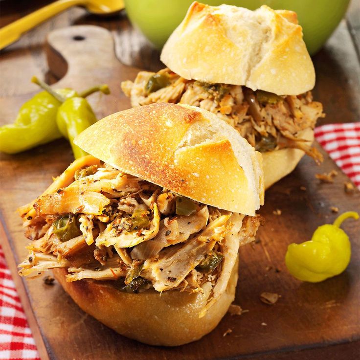 two pulled pork sandwiches sitting on top of a wooden cutting board next to green peppers