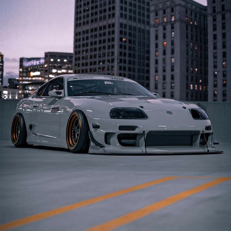 a white sports car parked in front of some tall buildings at night with lights on