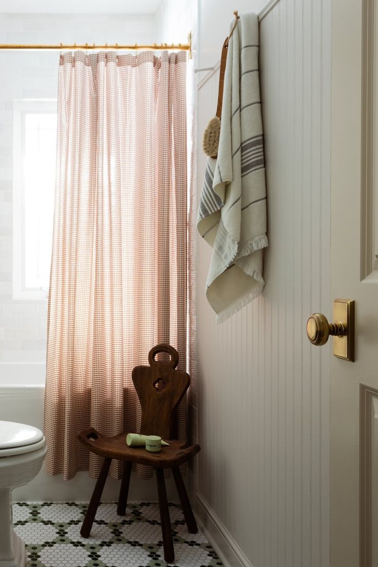 a white toilet sitting next to a wooden stool in a bathroom under a shower curtain