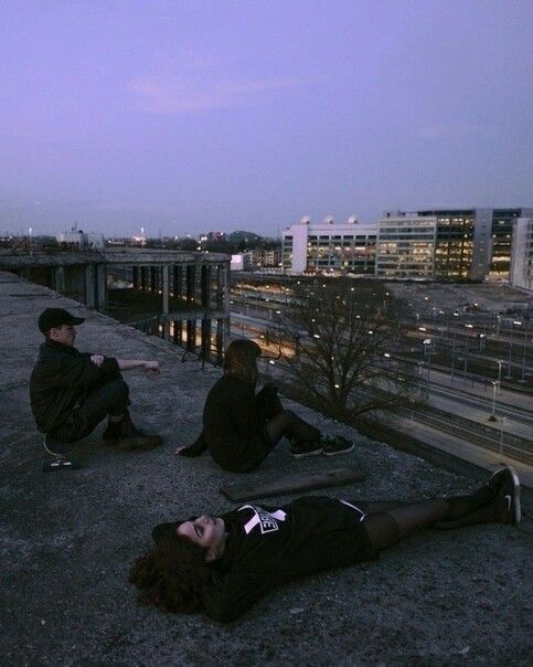 three people sitting on the roof of a building at night with city lights in the background