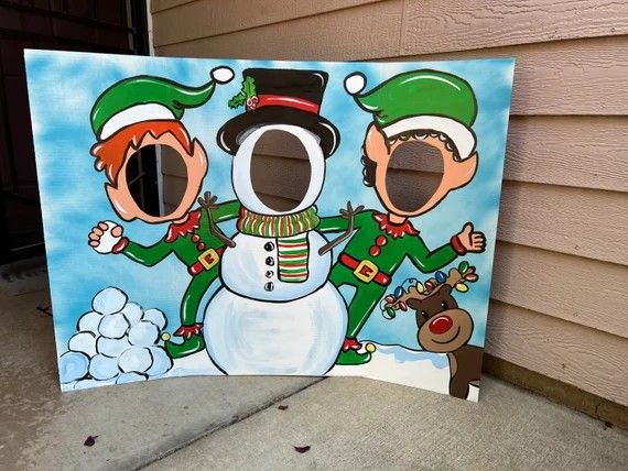 a snowman and two elfs are standing in front of a painting on the side of a house