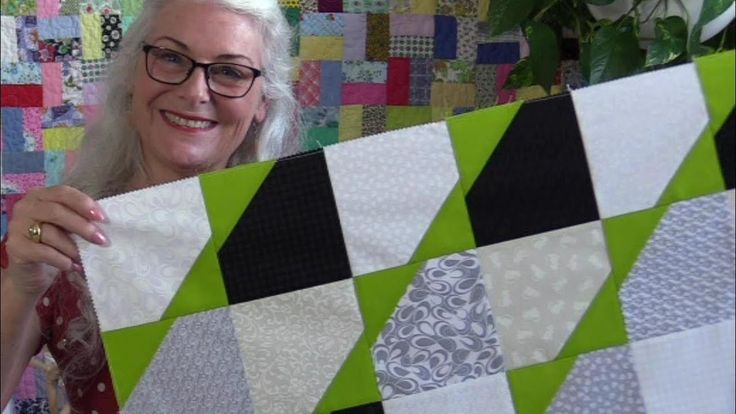 a woman holding up a quilt made with squares and strips in green, black, white and grey colors