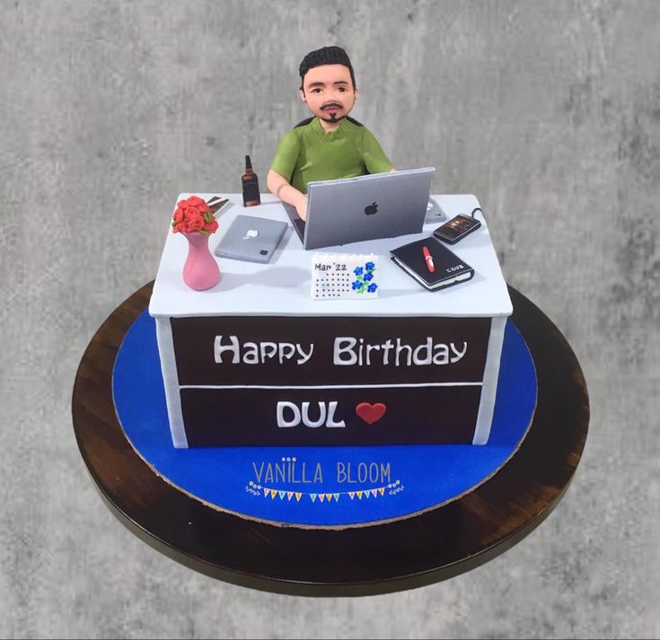 a birthday cake with a man sitting in front of a laptop on top of it