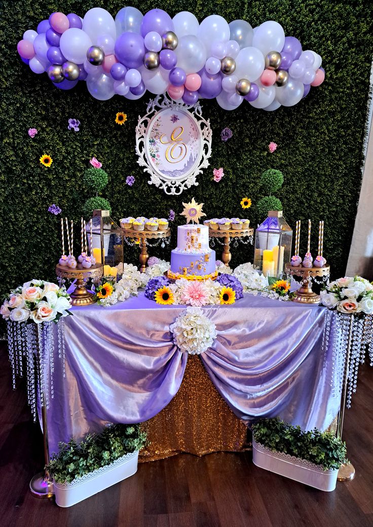 the table is covered with purple and white balloons, flowers, and cake for a princess themed birthday party