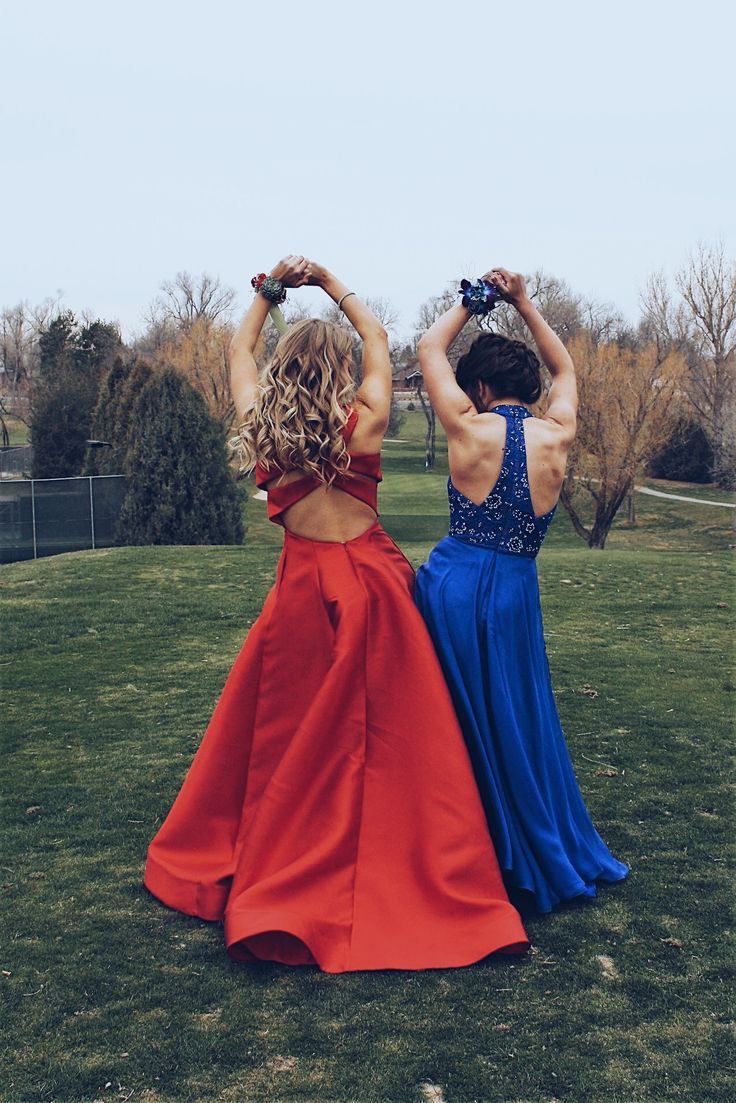 two women in red and blue dresses standing on the grass with their backs to each other