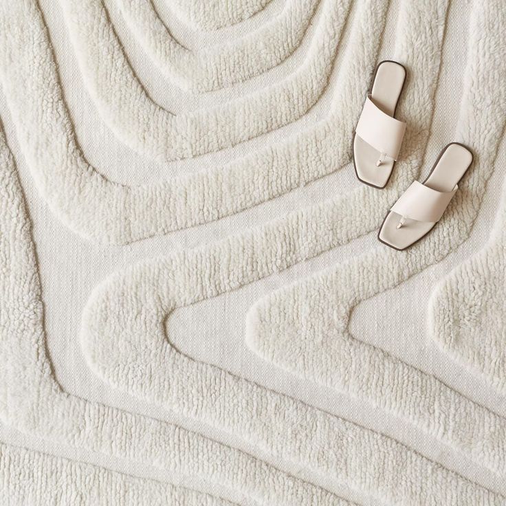 a pair of white slippers laying on top of a bed next to a rug