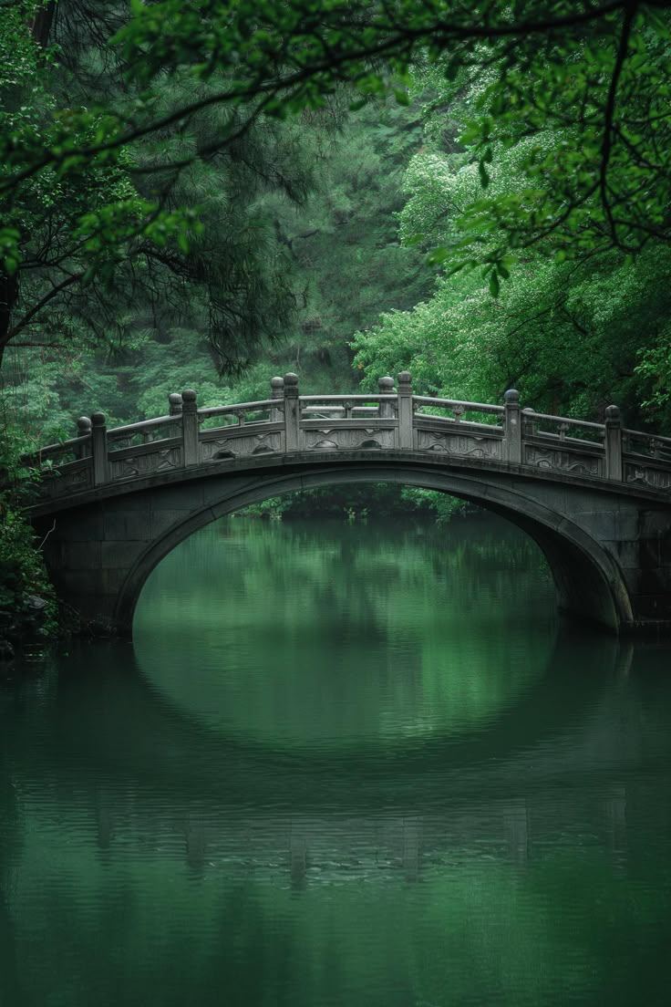 a bridge over a body of water surrounded by trees and greenery in the background