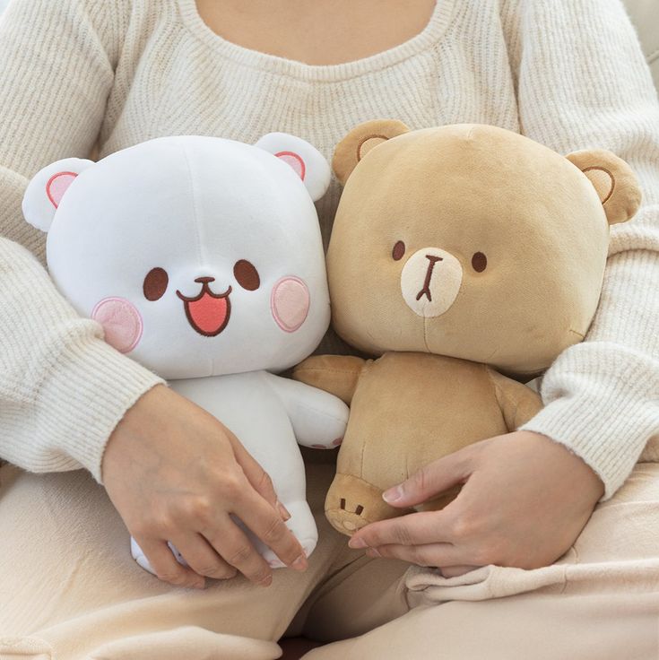 a woman holding two teddy bears in her arms while sitting on a couch with pillows