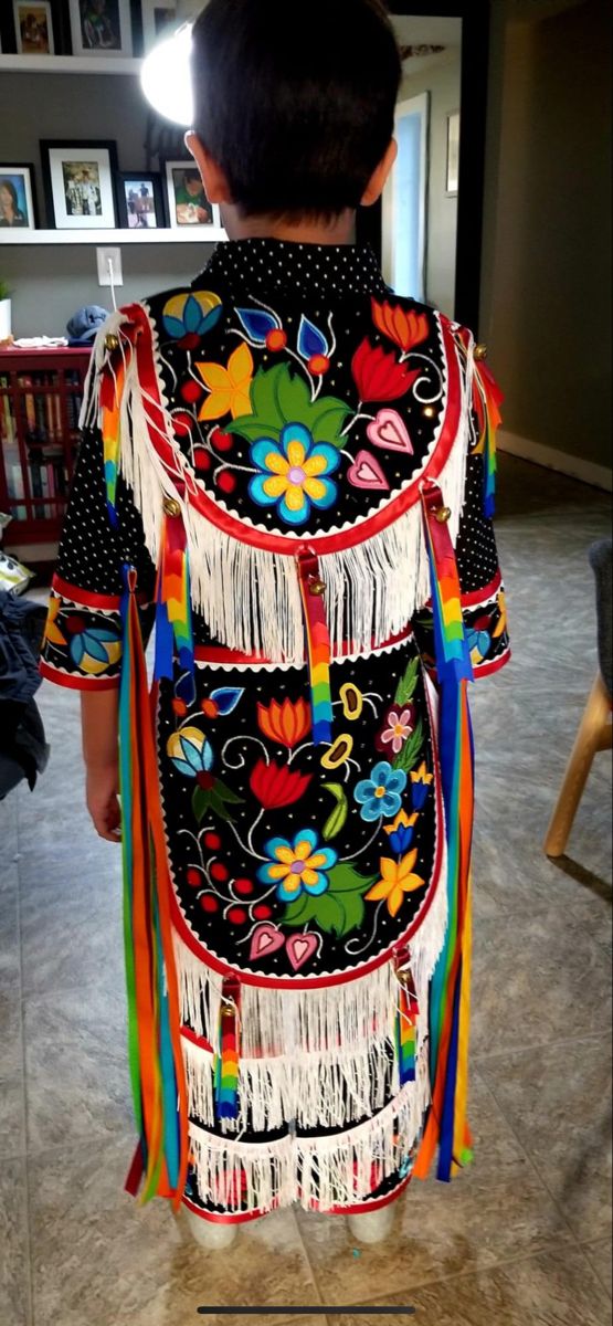 a young boy wearing a colorful dress with fringes