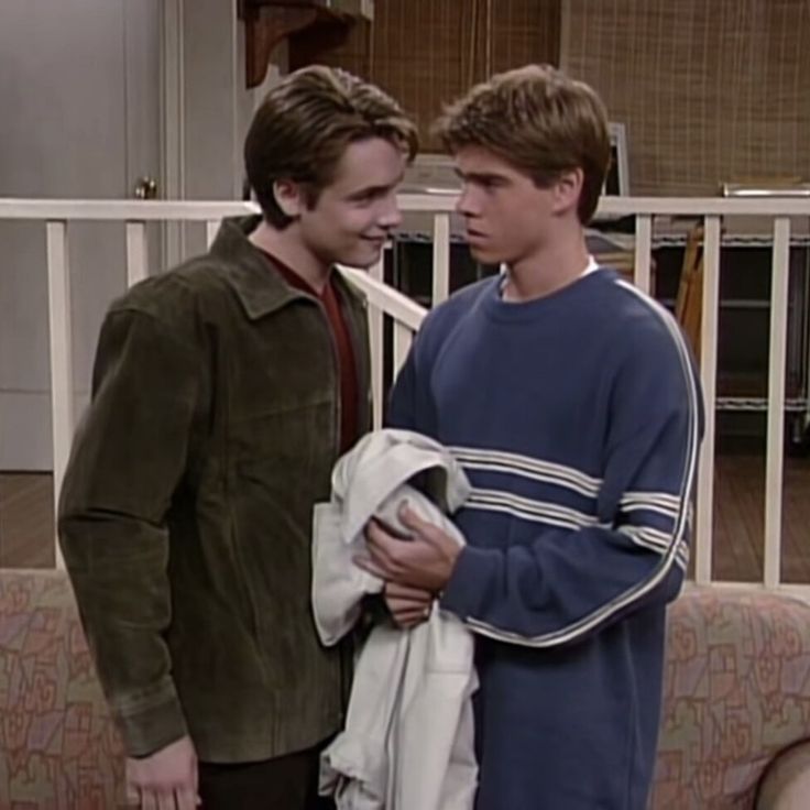 two young men standing next to each other in front of a couch and railings