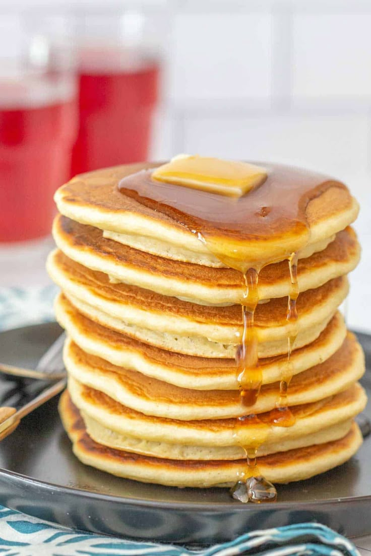 stack of pancakes covered in syrup on a black plate with blue and white napkins