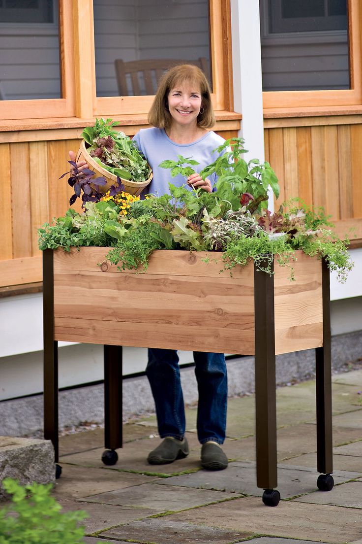 a woman standing in front of a planter filled with greens and vegetables on a patio