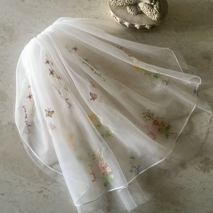 a white dress with flowers on it sitting next to a silver vase and an owl figurine