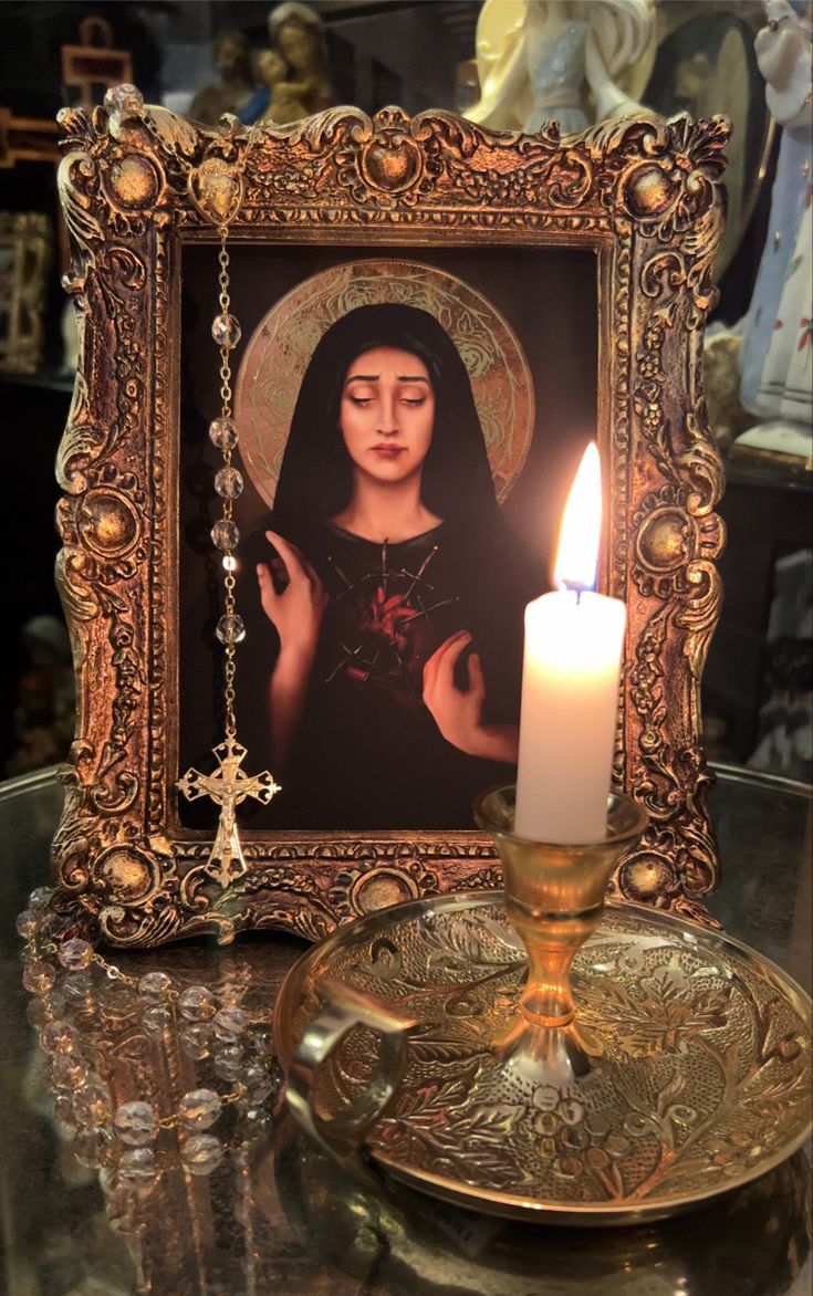 a lit candle sitting on top of a table in front of a picture frame with an image of the virgin mary