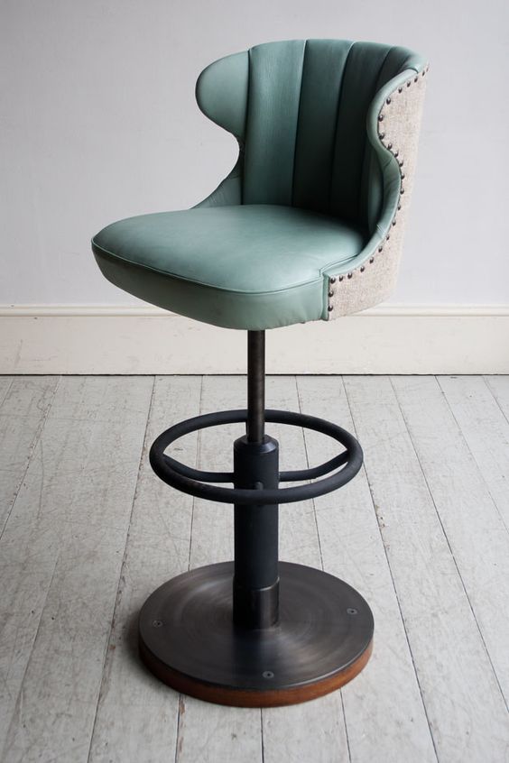 an upholstered bar stool with a blue seat and foot rest in front of a white wall