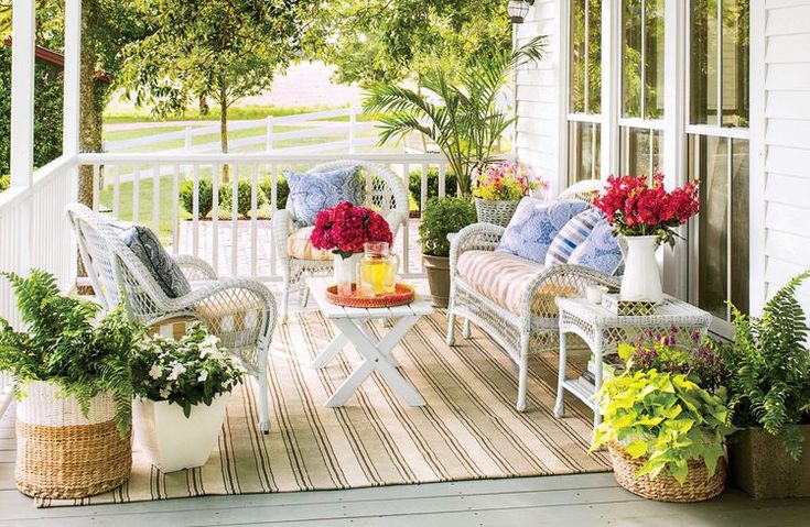 the porch is decorated with white wicker furniture and colorful potted plants on it