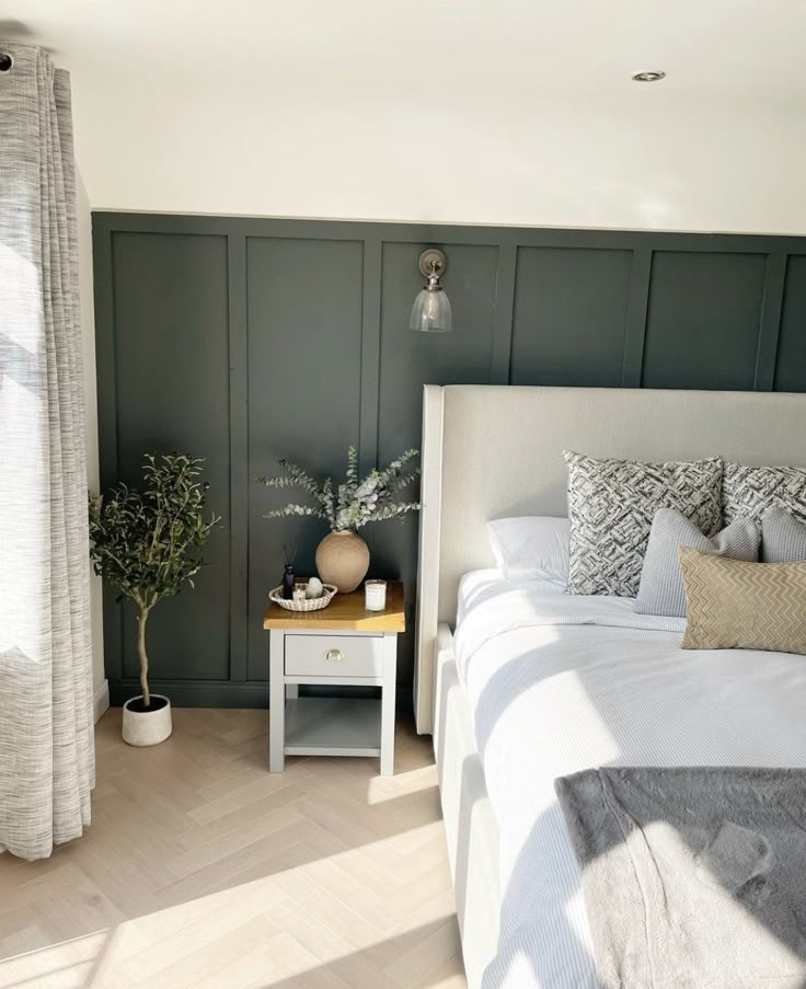 a white bed sitting in a bedroom next to a wooden table with two potted plants on it