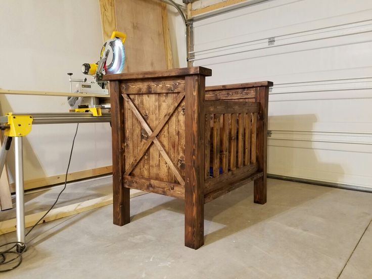 an unfinished wooden baby crib in a garage with a sawhorse on the side