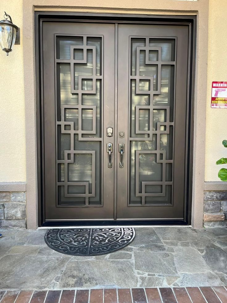 a pair of double doors in front of a house with brick walkway and door mat