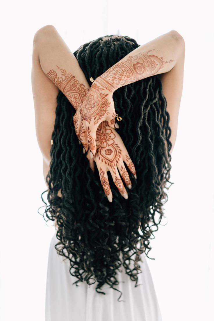 the back of a woman's head with henna tattoos on her arms and hands