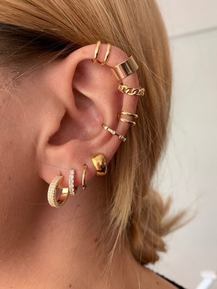 a close up of a person wearing gold ear cuffs and an ear cuff with five different designs