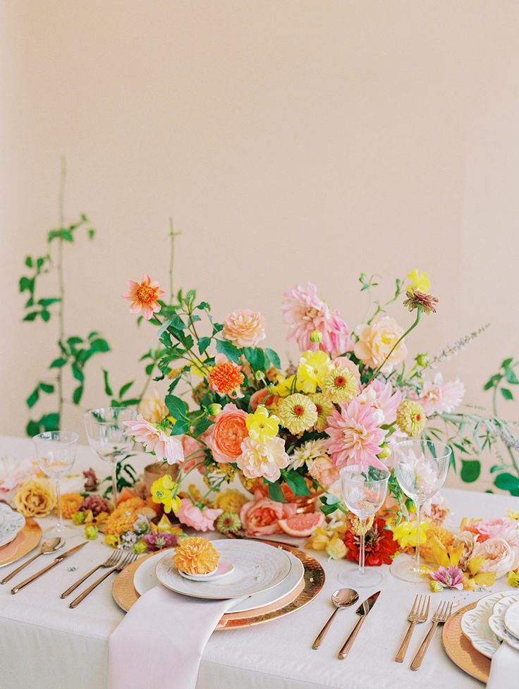 the table is set with plates, silverware and colorful flowers in vases on it